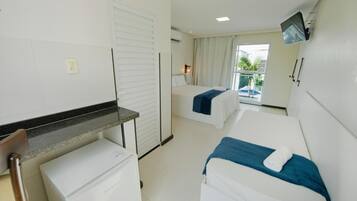 A hotel room with two beds, a small desk, a refrigerator, and a TV mounted on the wall.