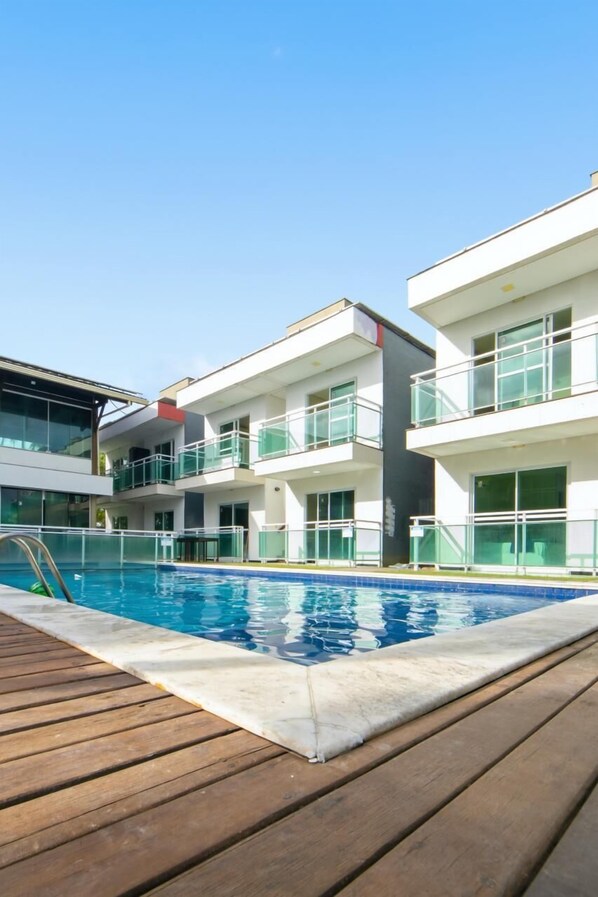 Un hotel moderno con piscina, terraza de madera y barandillas de vidrio.