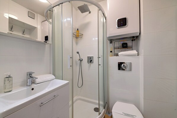 Un baño moderno con ducha de vidrio, un lavabo blanco con dispensador de jabón y un inodoro con etiqueta de desinfección.