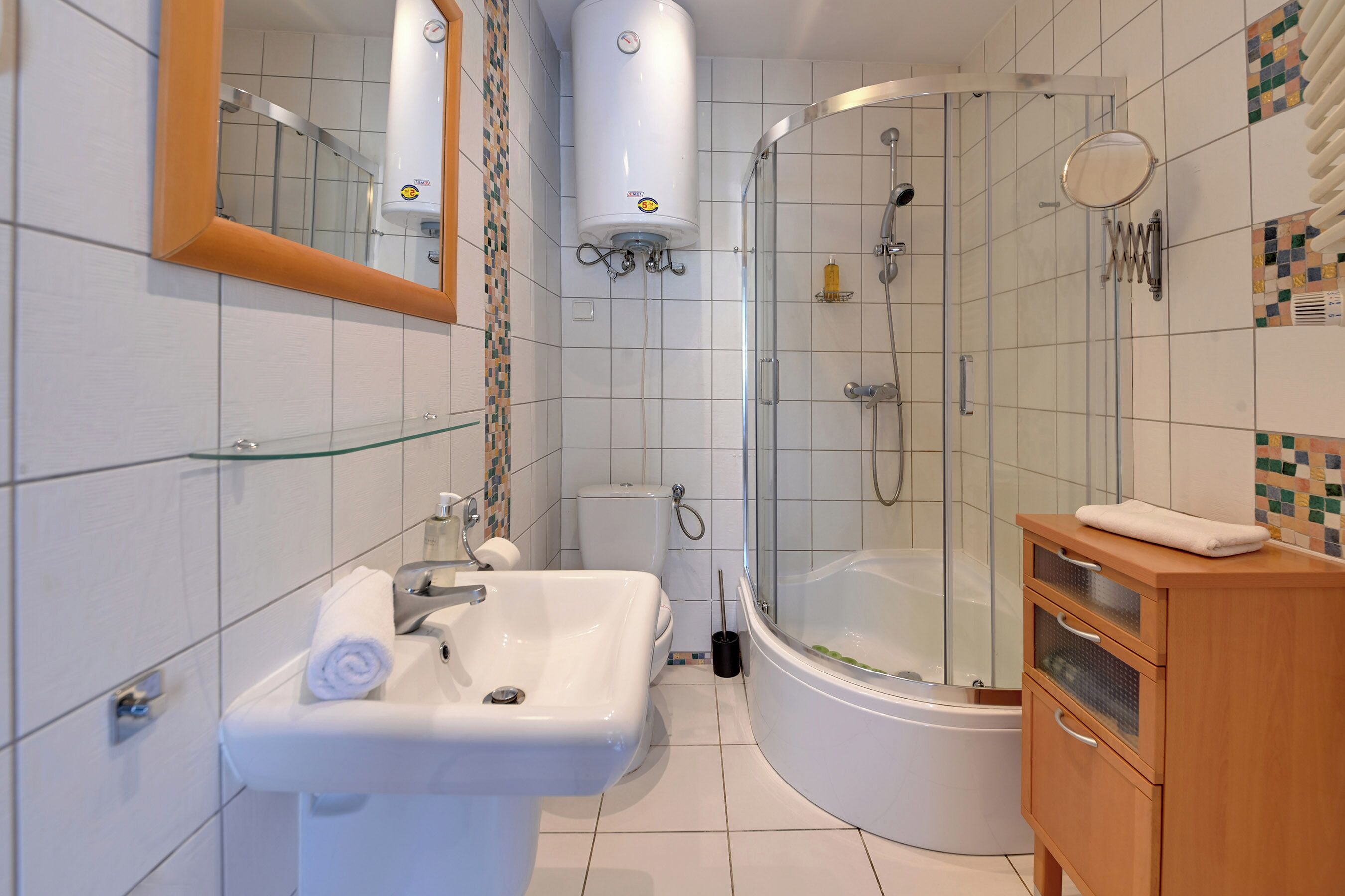 Een moderne badkamer met een glazen douchecabine, een witte wastafel en een houten meubel.