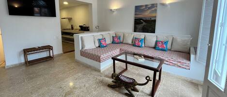 A living room with a sofa, a coffee table, and a TV. There is a staircase leading to an upper level.