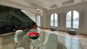 Een ruime kamer met een glazen tafel, moderne stoelen, een groot rondboogvenster en uitzicht op een stadsbeeld.