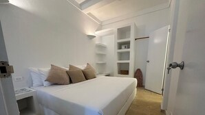 Een slaapkamer met een bed, witte muren, een inbouwkast en een deur.