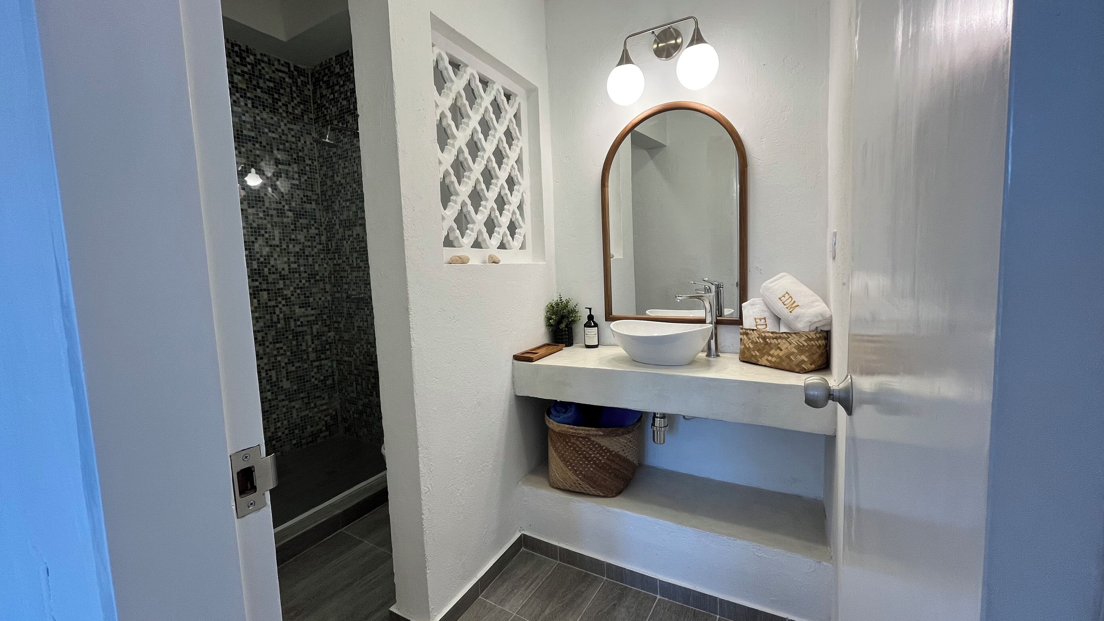 Une salle de bain avec un lavabo blanc, un grand miroir et une douche aux carreaux de mosaïque.