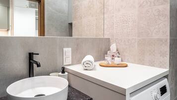 A modern bathroom with a sink, mirror, wall-mounted towel dispenser, and a front-loading washing machine.