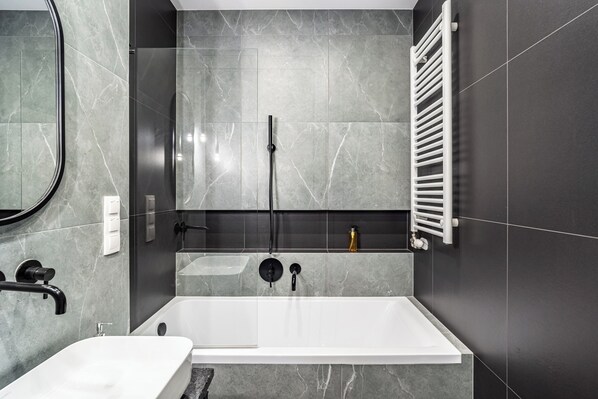 A modern bathroom with a bathtub, a shower, a sink, and a towel rack. - RentPlanet - Apartamenty przy Spodku (Katowice)