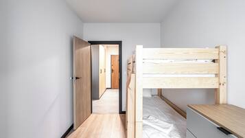 A narrow hallway with a bunk bed on the right, wooden flooring, and a door leading to another room.