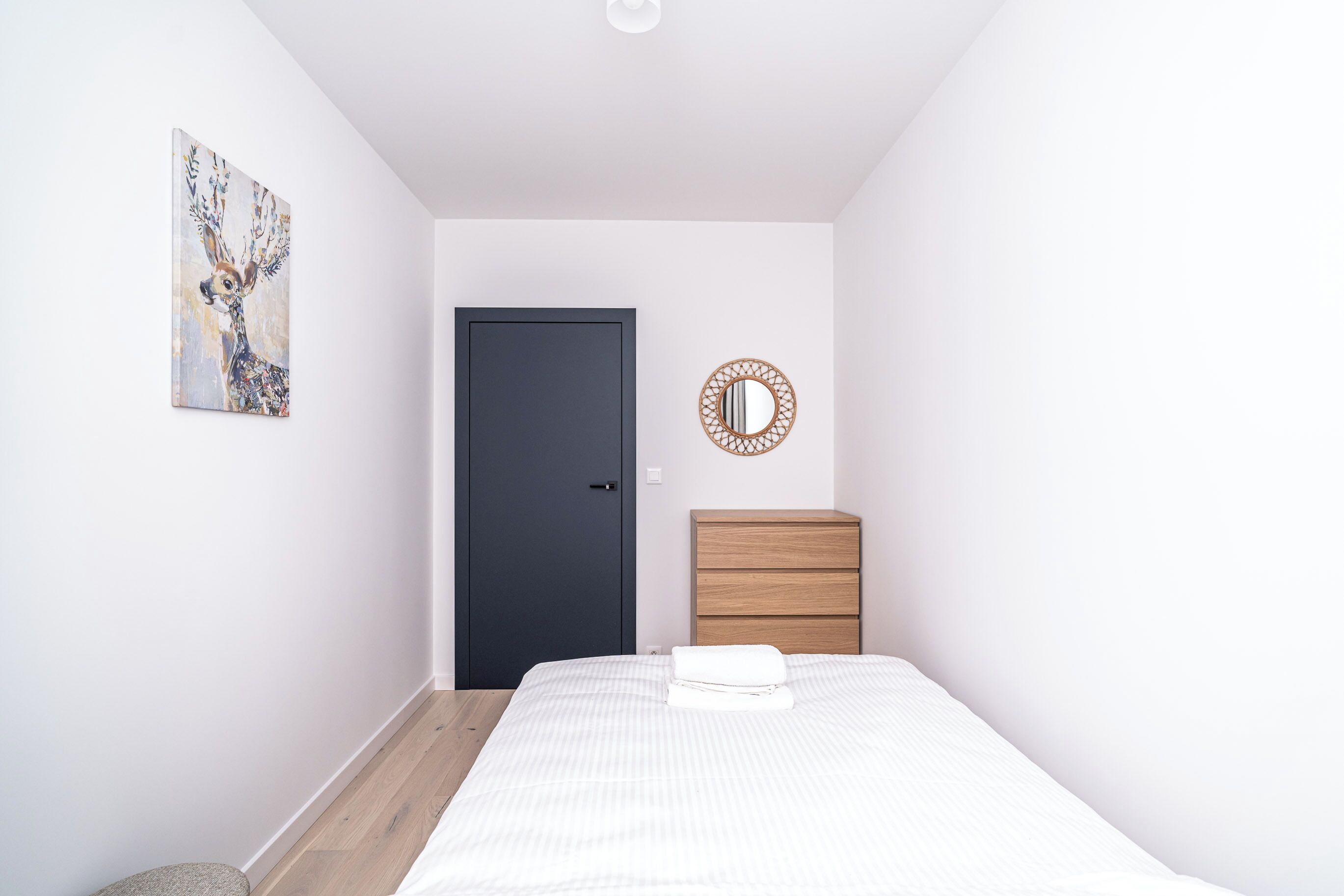 Un dormitorio con cama, cómoda, puerta y espejo fijado a la pared.
