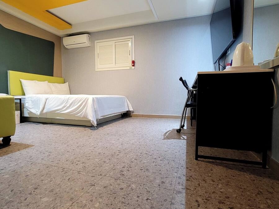 A hotel room with a bed, a desk, a chair, an air conditioning unit, and a television on the wall.
