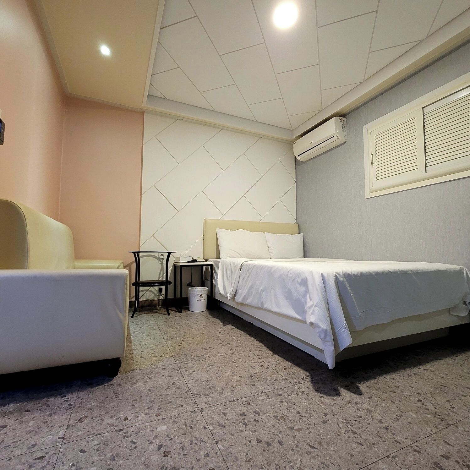 Una habitación de hotel con dos camas, una silla, una mesita y un equipo de aire acondicionado.