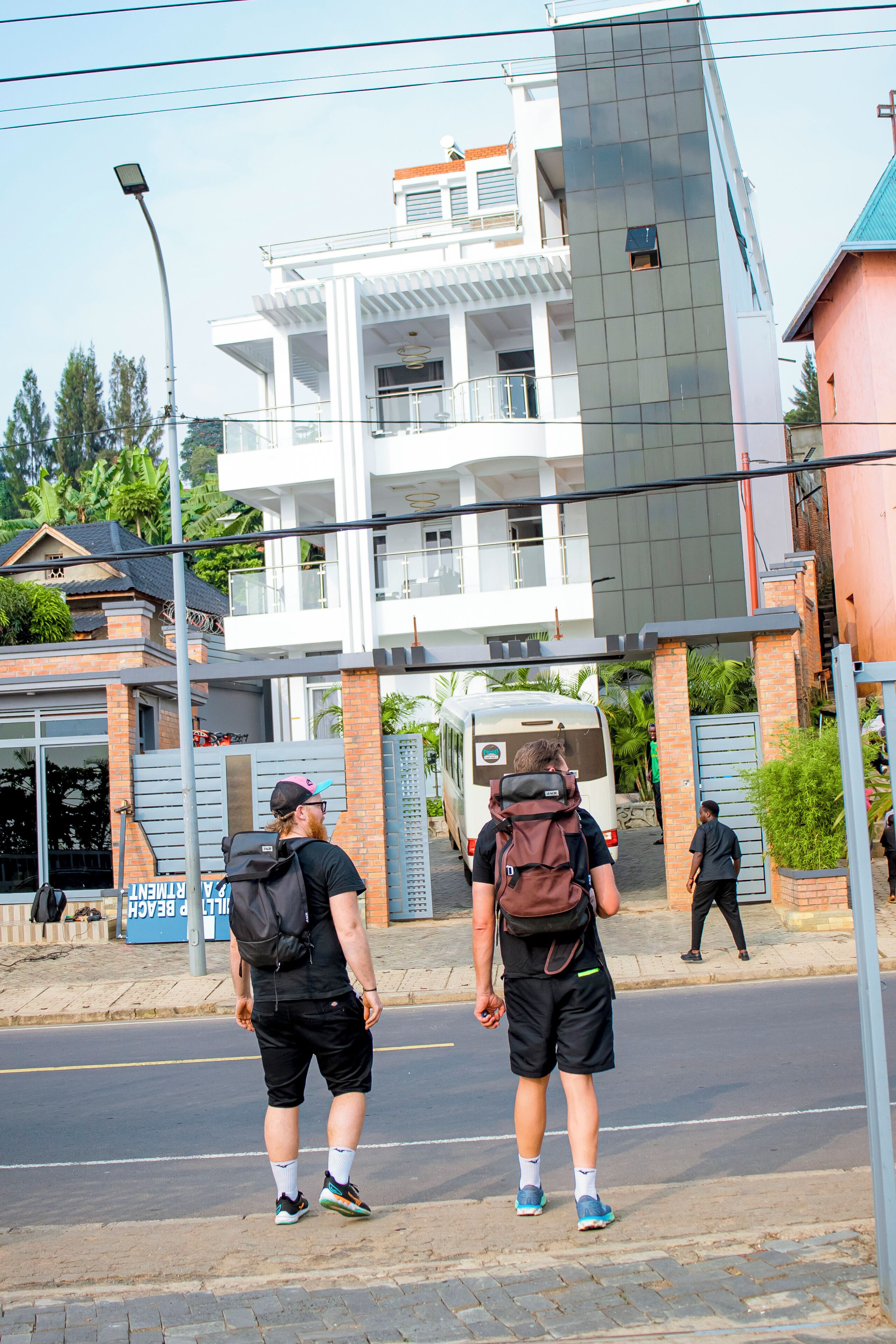 Duas pessoas na calçada, um ônibus ao fundo e um prédio moderno com varandas.