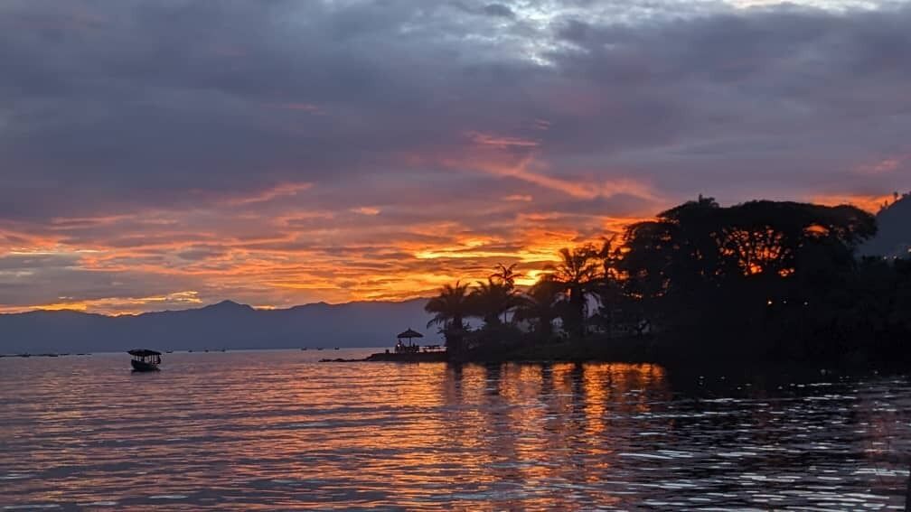 A sunset over a body of water with a boat and a distant structure.
