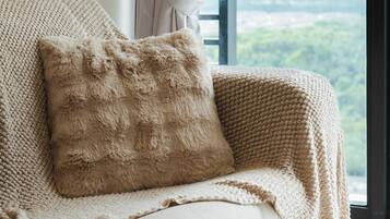 A cozy, knitted chair with a fluffy pillow, positioned near a window with a view of greenery.