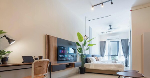 Une chambre d’hôtel moderne, équipée d’un lit, d’un bureau avec un ordinateur portable, d’une télévision, d’une plante en pot et d’une fenêtre.