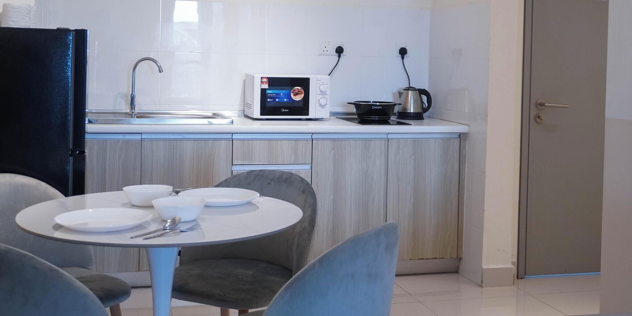 Een moderne keuken met een magnetron, waterkoker en een eettafel, compleet met borden en bestek.