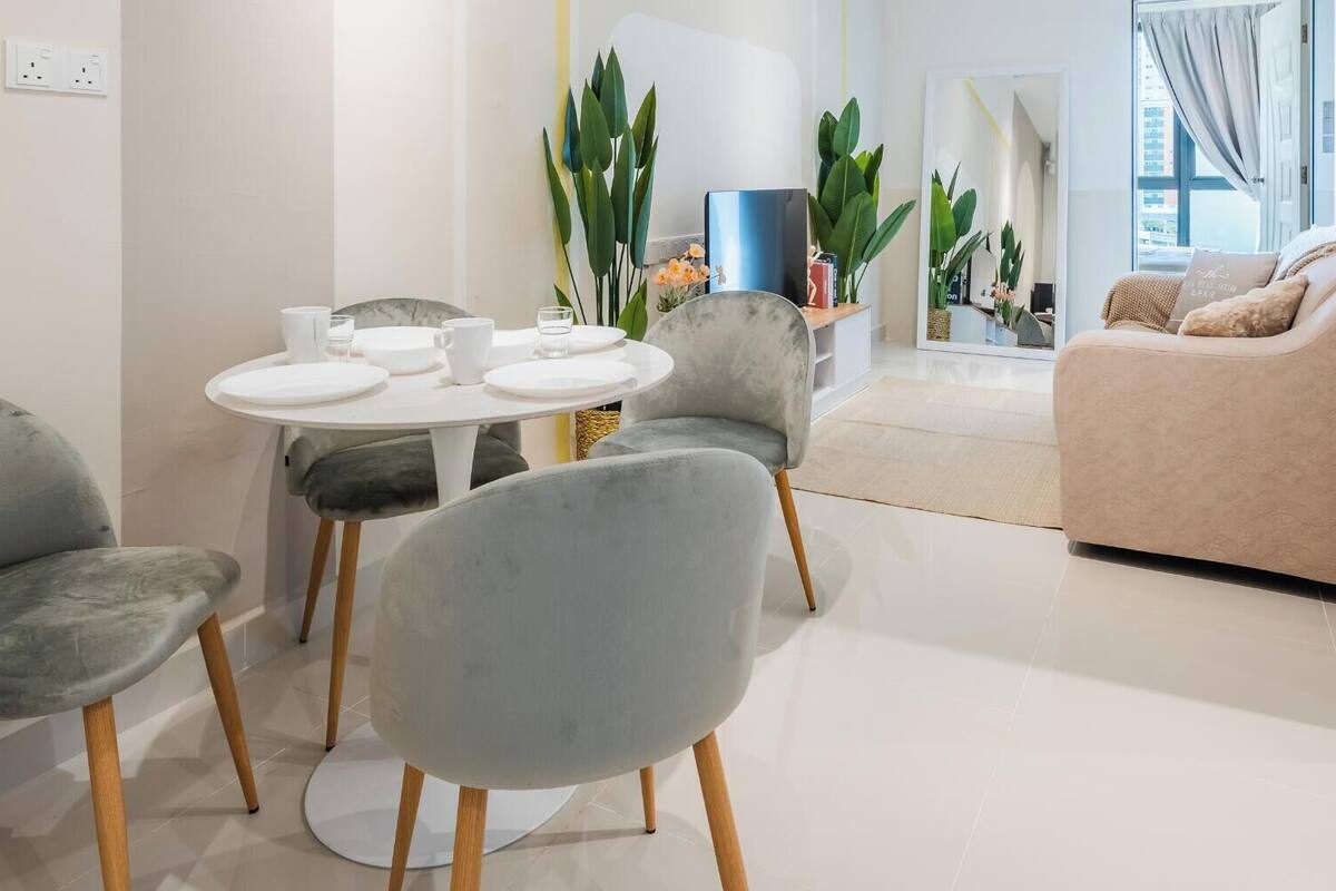 A modern living room with a round dining table, grey upholstered chairs, a beige sofa, and a large mirror reflecting the room.