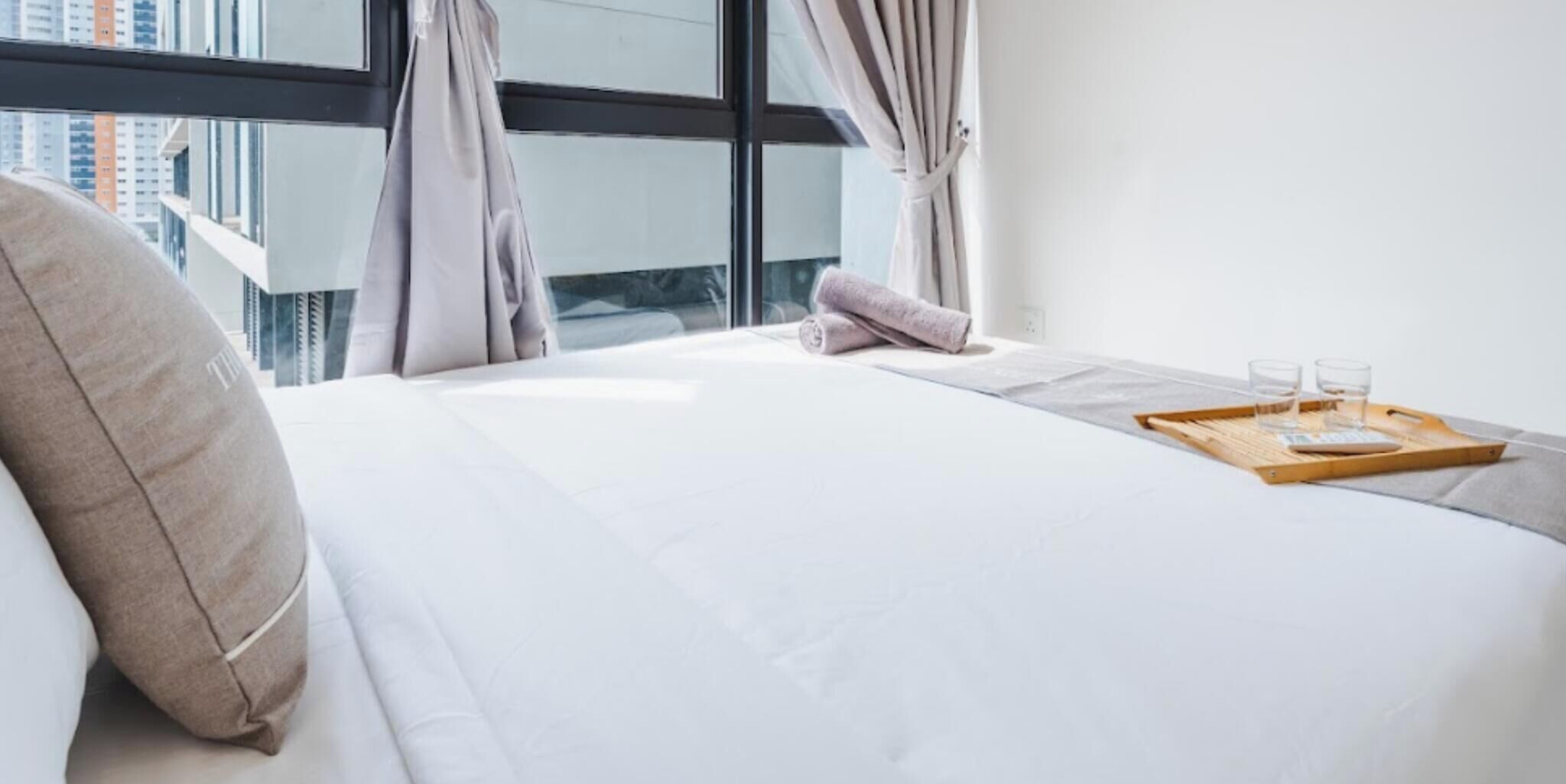 Une chambre d’hôtel avec un grand lit, une fenêtre avec des rideaux et un plateau avec des verres et une bouteille.