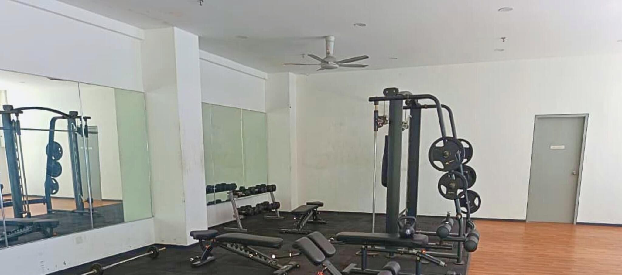 A gym with weightlifting equipment, mirrors, and a ceiling fan.