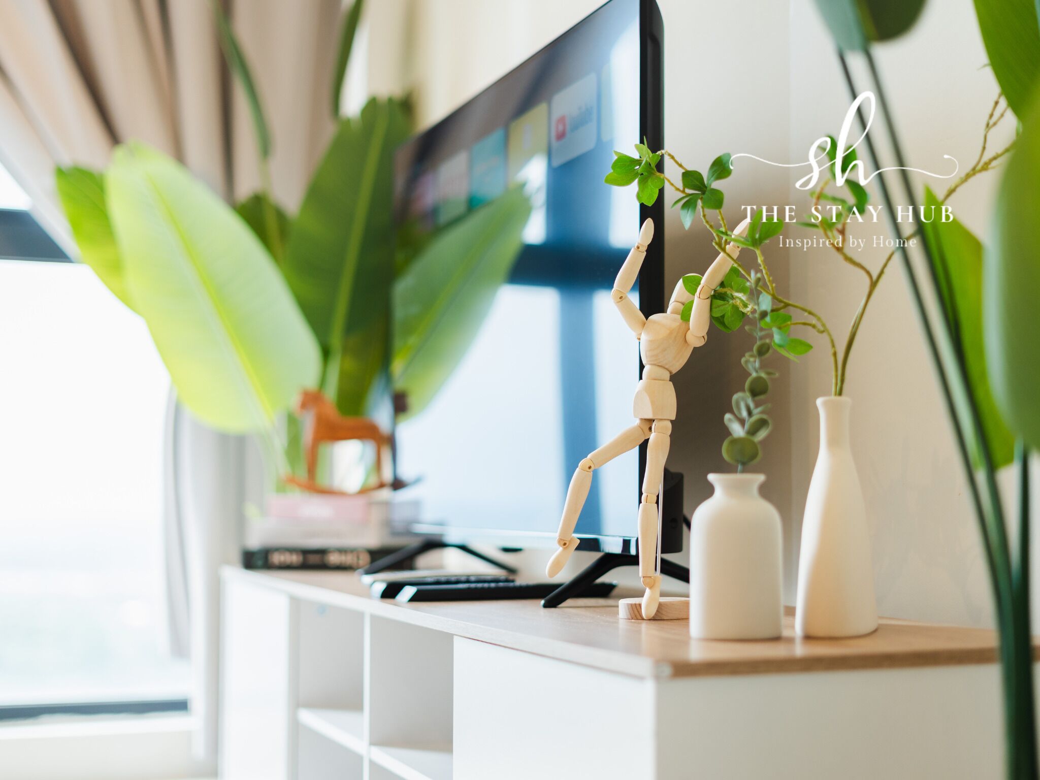 A wooden mannequin on a shelf with a plant, a TV, and a vase.