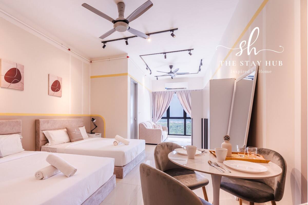 A hotel room with two beds, a dining table with chairs, a ceiling fan, and artwork on the walls.