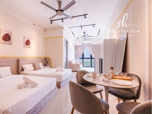 Une chambre d’hôtel avec deux lits, une table à manger avec des chaises, un ventilateur de plafond et des œuvres d’art accrochées aux murs.