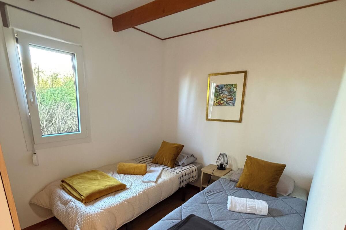 A room with two beds, a window, a framed picture, and a bedside table.
