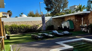A swimming pool with lounge chairs, a stone wall, and a pergola.