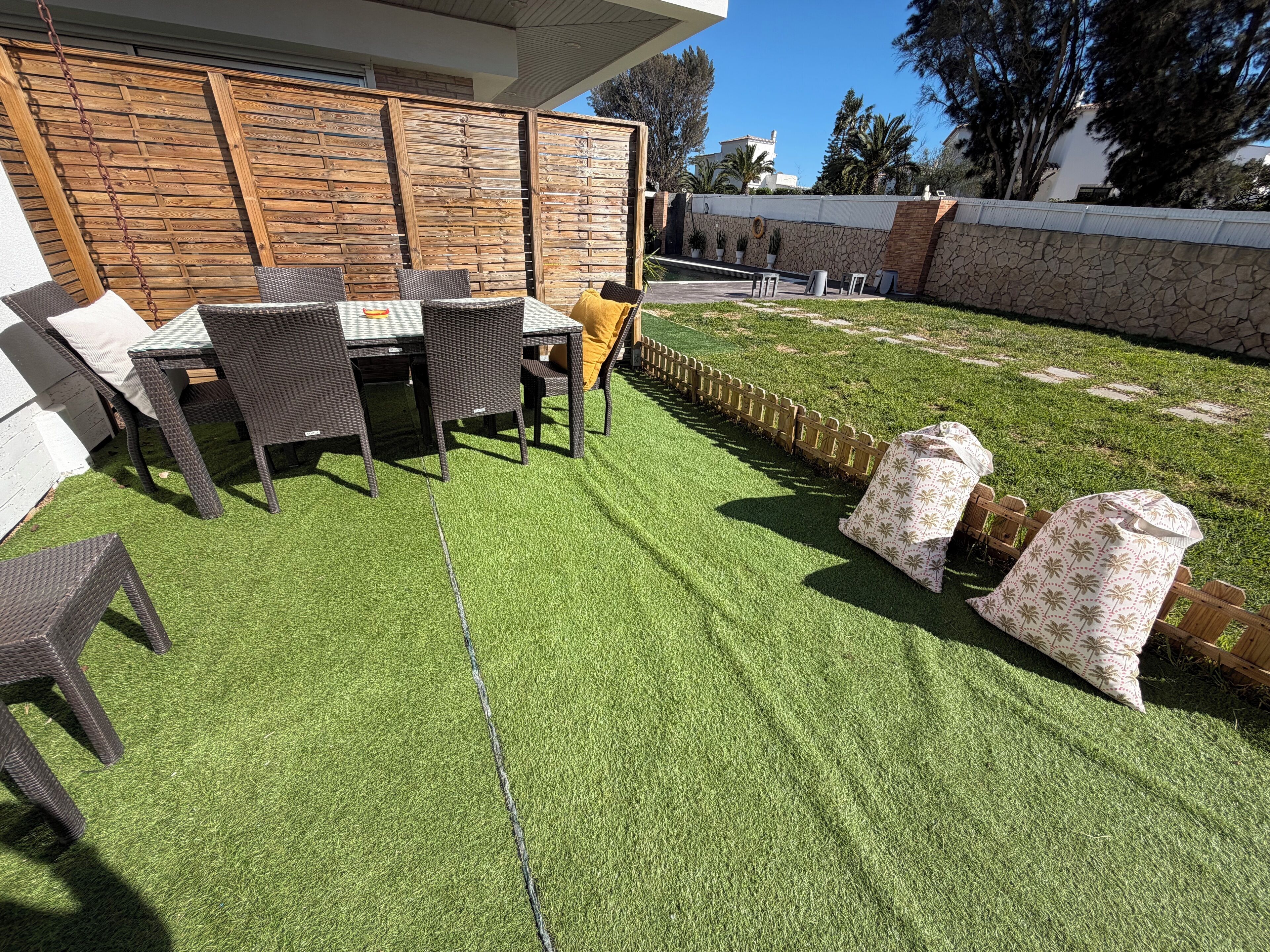Un patio al aire libre con mobiliario de mimbre, una valla de madera y un muro de piedra.