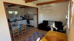 A compact room with a bed, a sofa, a dining table with chairs, and a kitchenette.