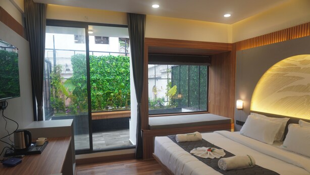 Habitación de hotel moderna con una cama grande, un escritorio y vistas a zonas verdes por las ventanas.