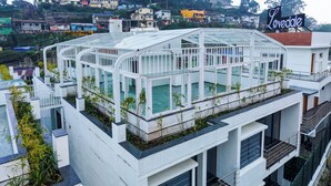 Un edificio moderno con una estructura de invernadero de vidrio en la azotea, rodeado de edificios urbanos.