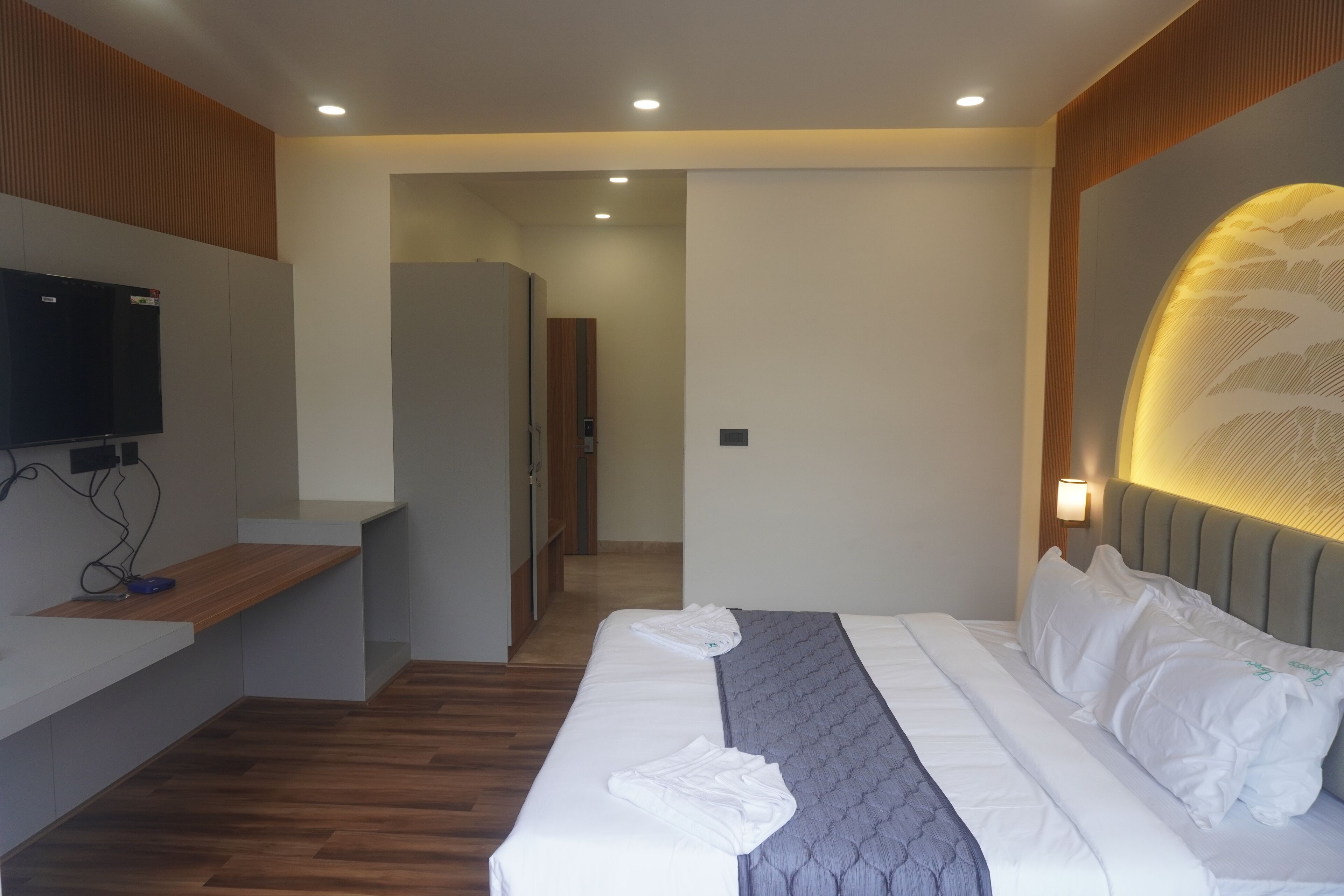 A modern hotel room with a neatly made bed, a flat-screen TV mounted on the wall, and a wooden bench.