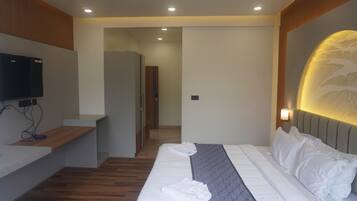 A modern hotel room with a neatly made bed, a flat-screen TV mounted on the wall, and a wooden bench.