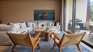 Uma sala de estar moderna com um sofá branco, duas cadeiras de madeira, uma mesa de centro e um quadro com barcos na parede.