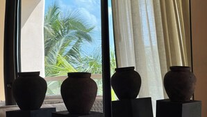 Três vasos sobre pedestais, perto de uma janela com vista para palmeiras.