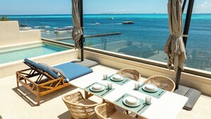 Piscina infinita no terraço com uma mesa posta para refeições, com vista para um mar azul e transparente com barcos.