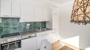 Eine moderne Küche mit weißen Schränken, einer grünen Fliesenrückwand, Edelstahlgeräten und einer Pendelleuchte.
