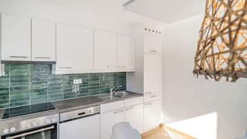 A modern kitchen with white cabinets, a green tiled backsplash, stainless steel appliances, and a hanging light fixture.