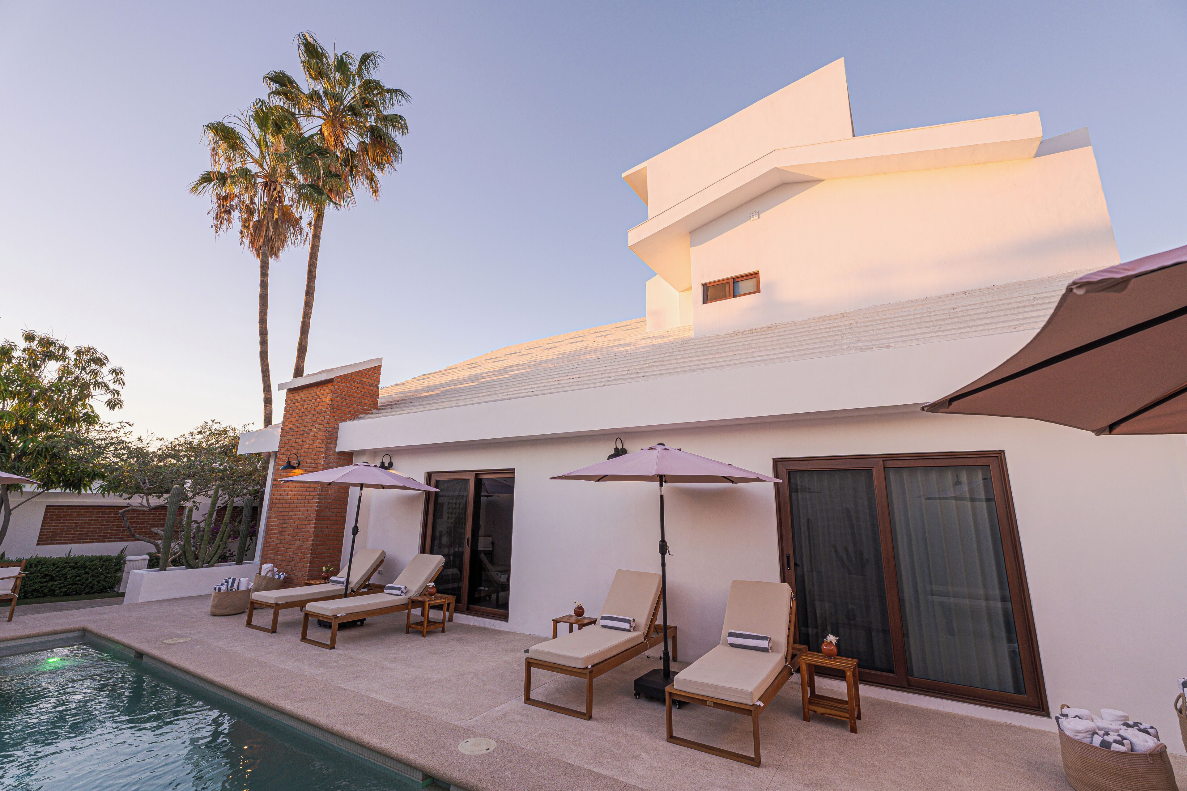 A modern building with a pool, lounge chairs, and umbrellas.
