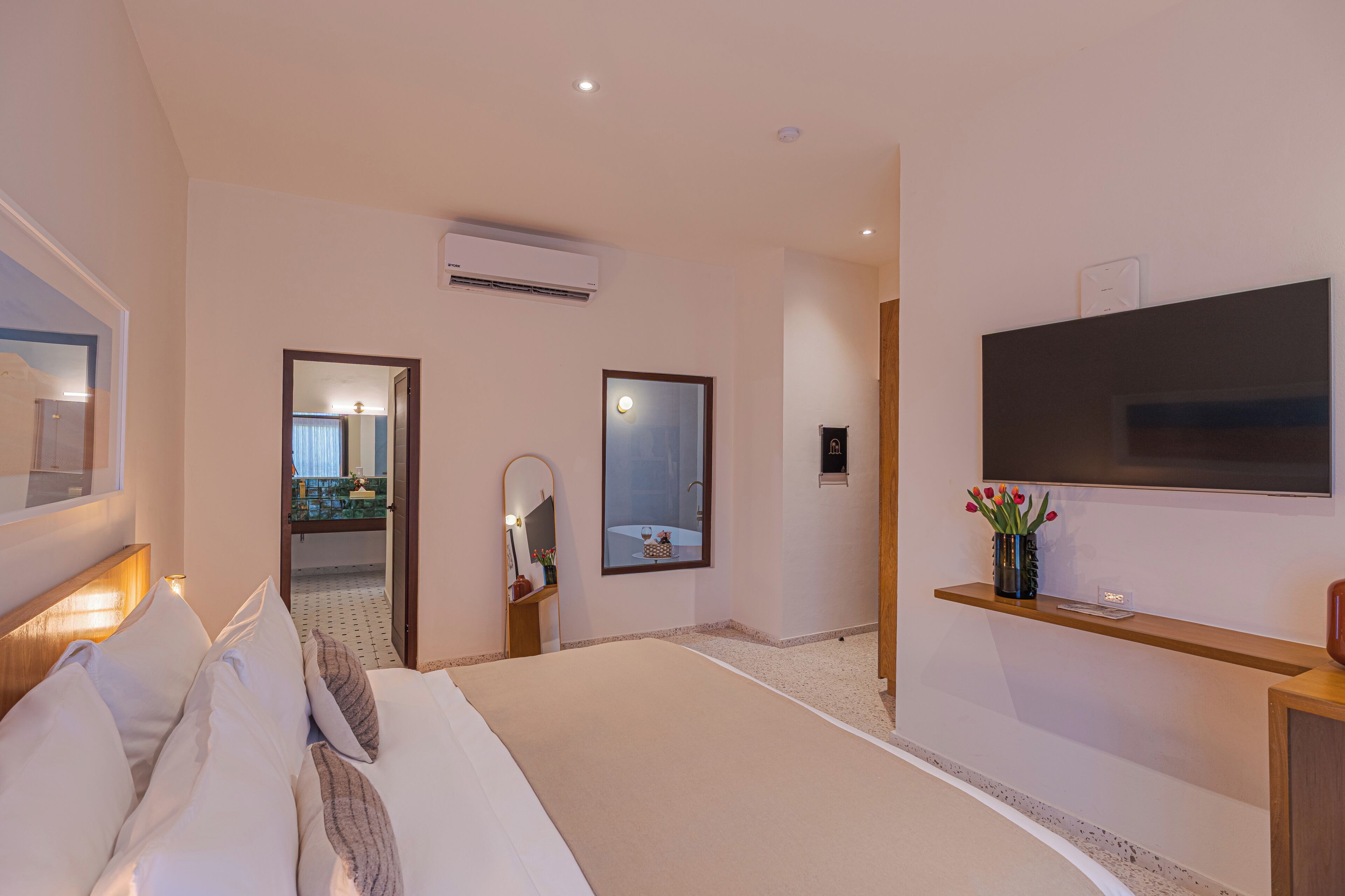 Een hotelkamer met een bed, een televisie, een spiegel en een klein tafeltje met een bloevas.