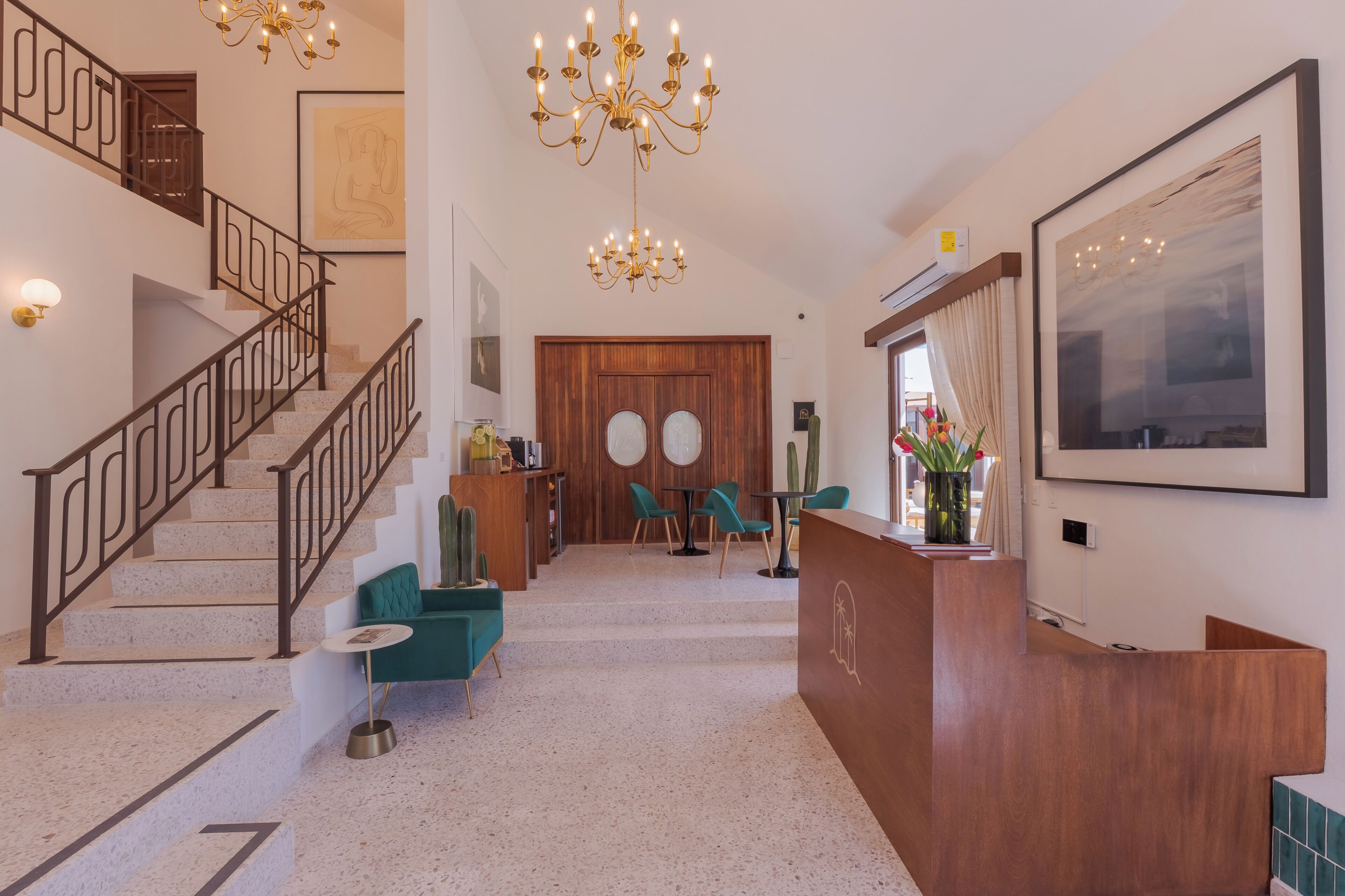 A hotel lobby with a staircase, a reception desk, teal chairs, a chandelier, and artwork on the walls.