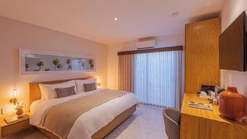 A hotel room with a bed, bedside table, desk, chair, and a large window with curtains.