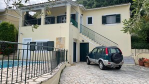 A two-story house with a stone-paved driveway and a car parked in front. - Villa Victoria (Corfu)