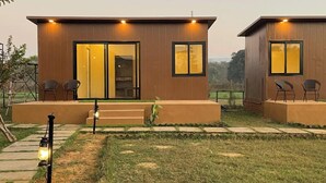 Un bâtiment moderne à deux étages, doté de grandes portes et fenêtres en verre, d’un petit espace extérieur aménagé avec des chaises, et d’un chemin menant à l’entrée.