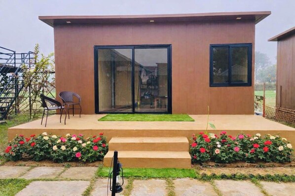 A modern building with a flat roof, large sliding glass doors, and a small outdoor seating area with two chairs. - Leopard Valley (Mathura)