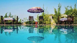 Une piscine aux eaux cristallines, dotée d’une terrasse en bois, entourée d’une végétation luxuriante et ombragée par des parasols.