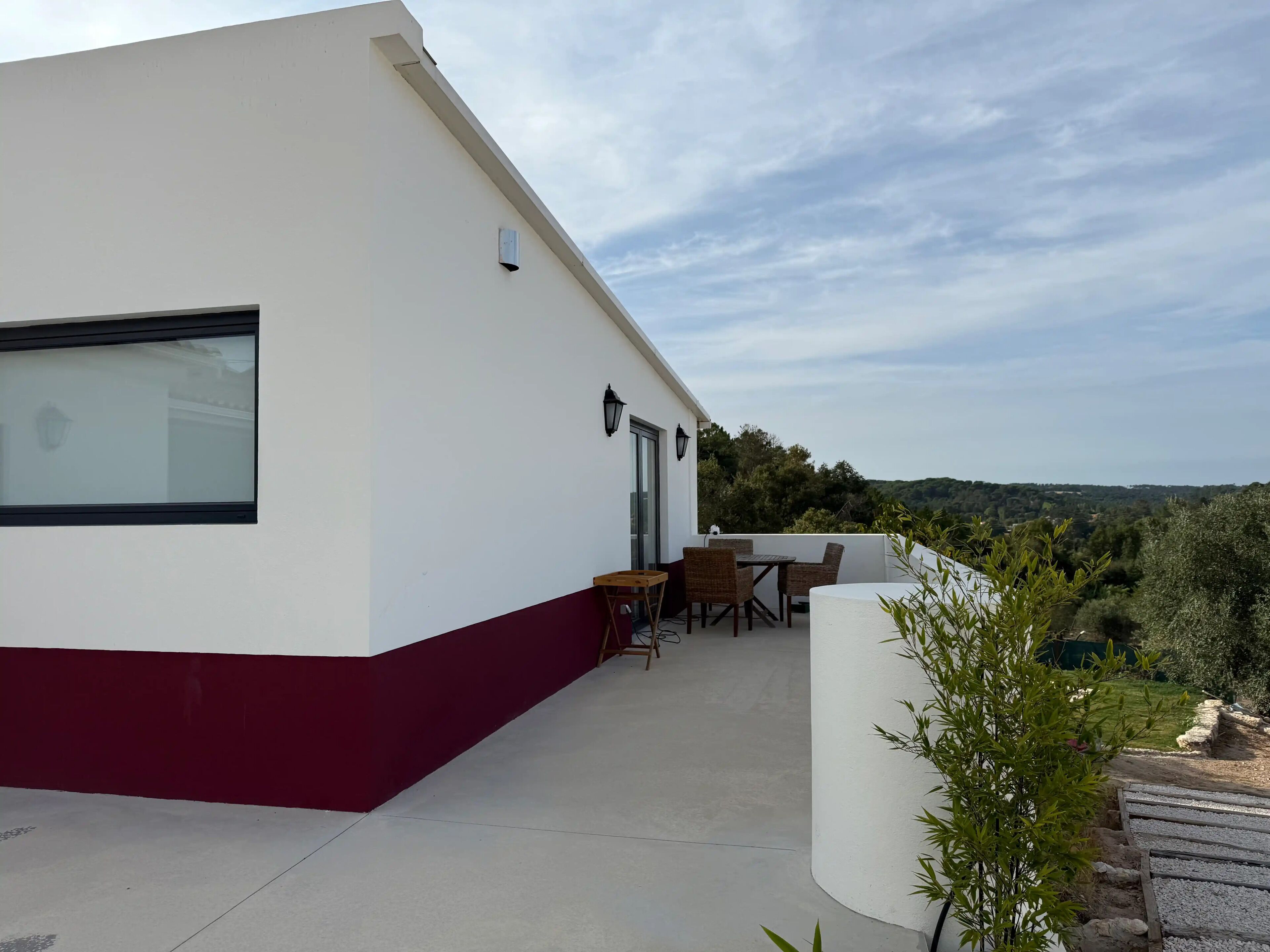 Un edificio moderno con fachada blanca y base roja, que cuenta con un patio amoblado y vistas del paisaje circundante.