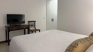 Un dormitorio con una cama, un televisor sobre un aparador de madera, una silla y un armario.