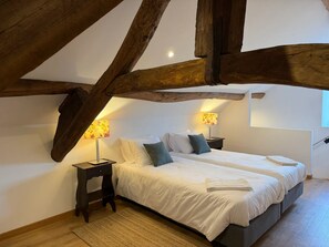 Quarto com duas camas, vigas de madeira, mesa de cabeceira com abajur e uma janela.