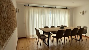 Un comedor con mesa y sillas de madera, un jarrón decorativo y una ventana con cortinas traslúcidas.